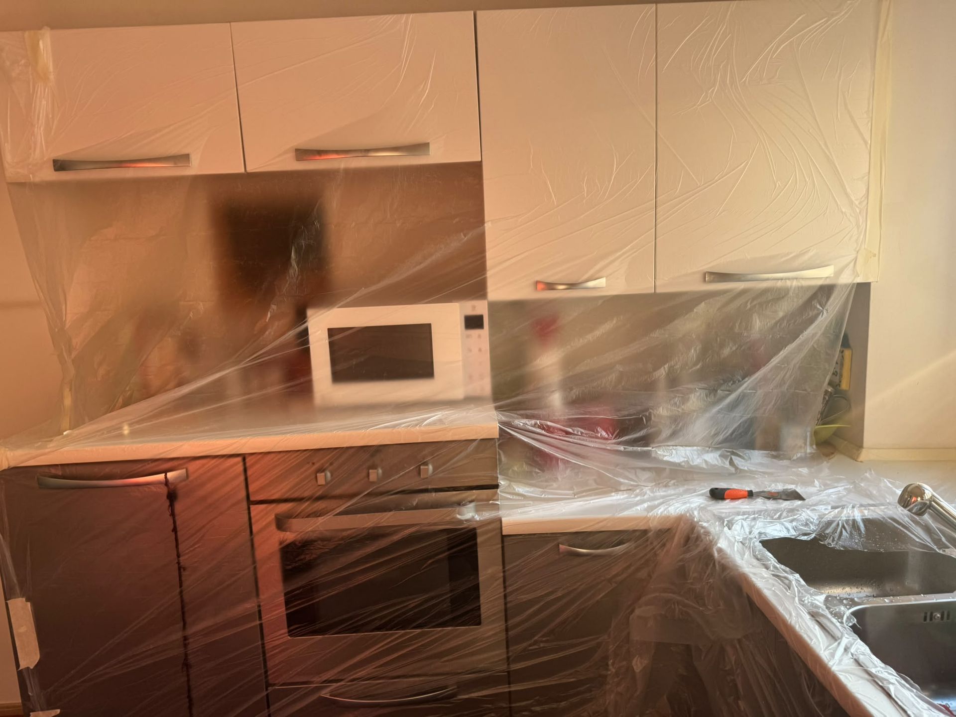 Cucina con mobili bianchi, paraschizzi in acciaio inox ed elettrodomestici coperti con teli
