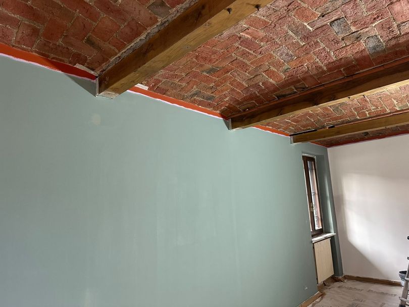 Stanza vuota con soffitto in mattoni a vista, parete verde chiaro e una piccola finestra sulla destra.