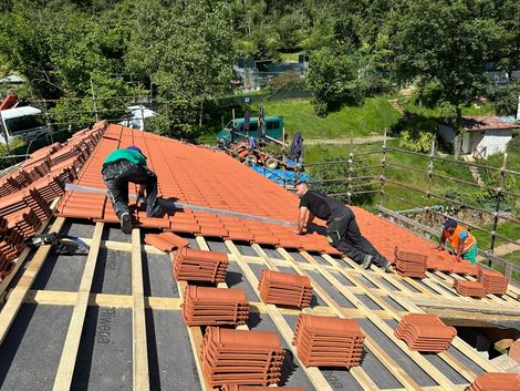 Operai installano tegole rosse su un tetto spiovente in una zona rurale verde
