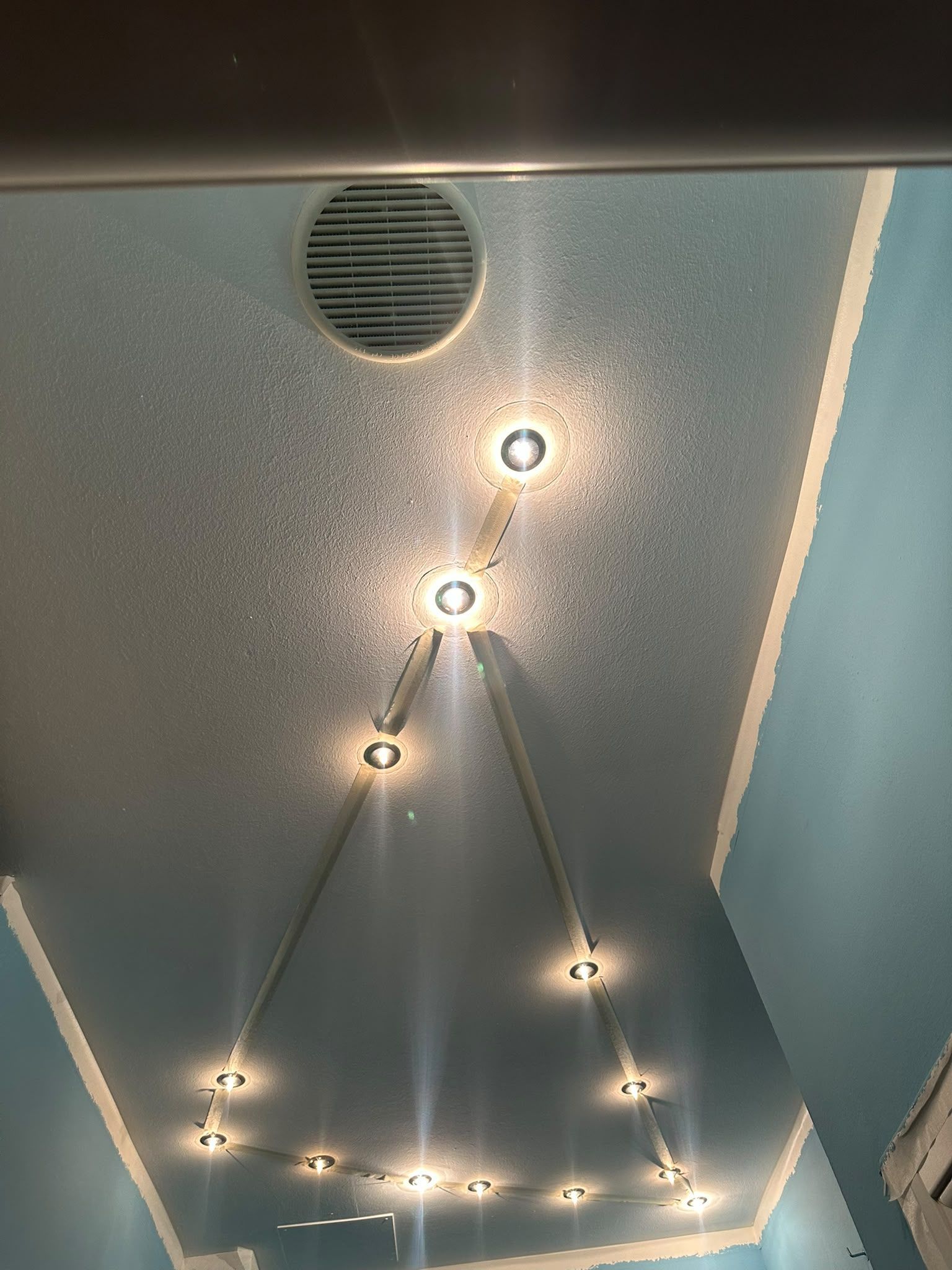 Soffitto con bocchetta di aerazione circolare e file di piccole lampade a sospensione su pareti color verde acqua