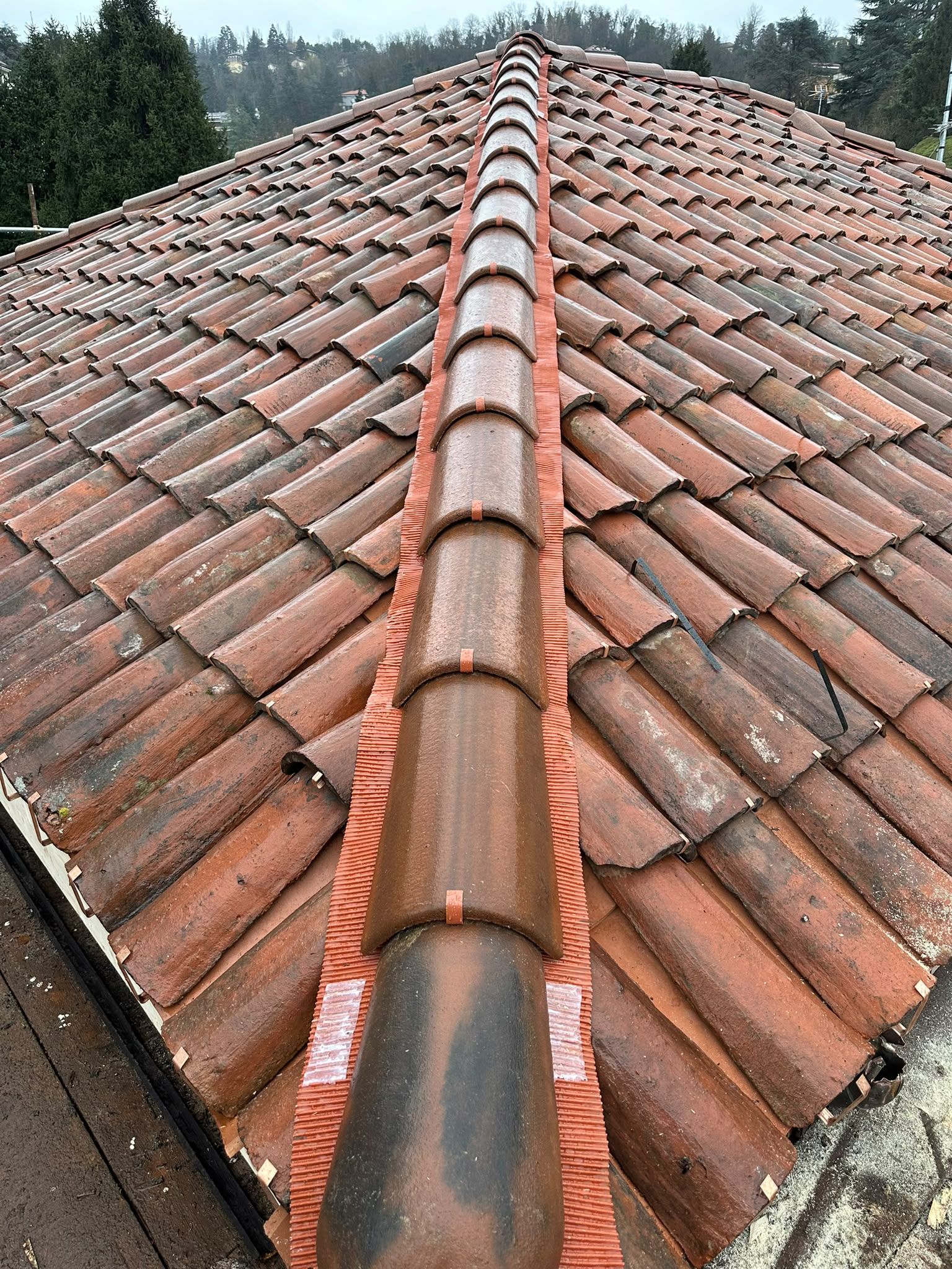 Tetto di tegole in terracotta con una presa d’aria centrale sul colmo, visto dall’alto in una giornata nuvolosa