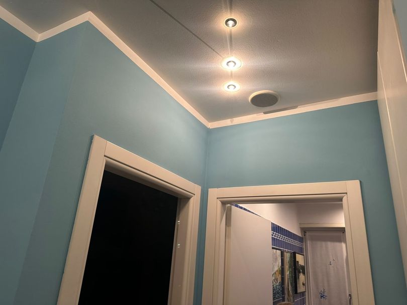 Corridoio con pareti azzurre, finiture bianche, faretti a incasso nel soffitto e una porta aperta.