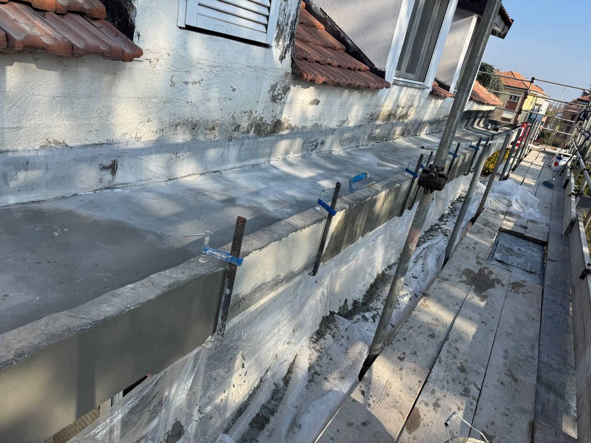 Stretto passaggio sul tetto accanto a un edificio fatiscente, con impalcature e lunghe ombre lungo il percorso