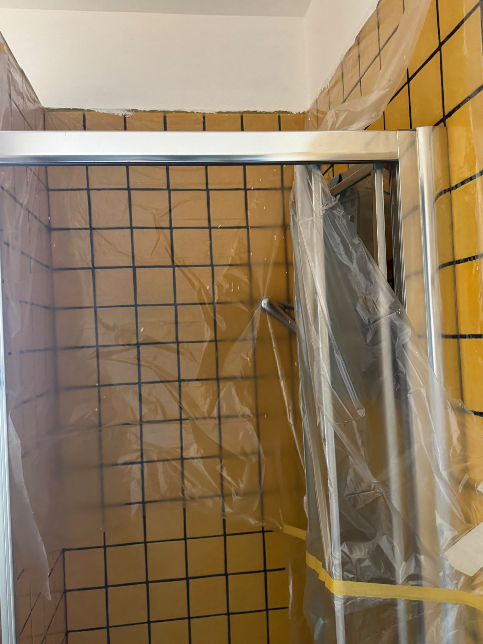Box doccia piastrellato con recinzione in rete metallica e apertura della porta coperta di plastica