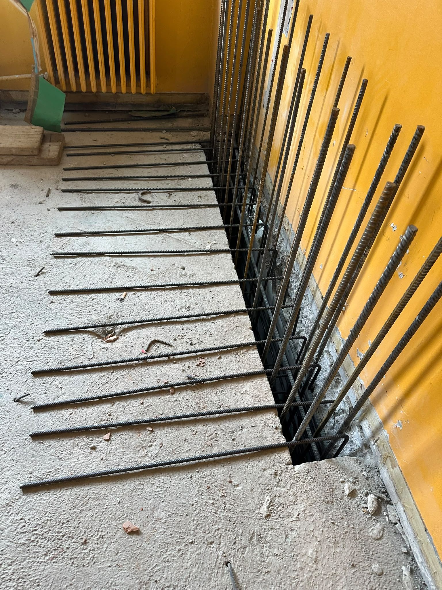 Materiali di scarto edili ostruiscono uno stretto passaggio pedonale accanto a un muro giallo e a pannelli