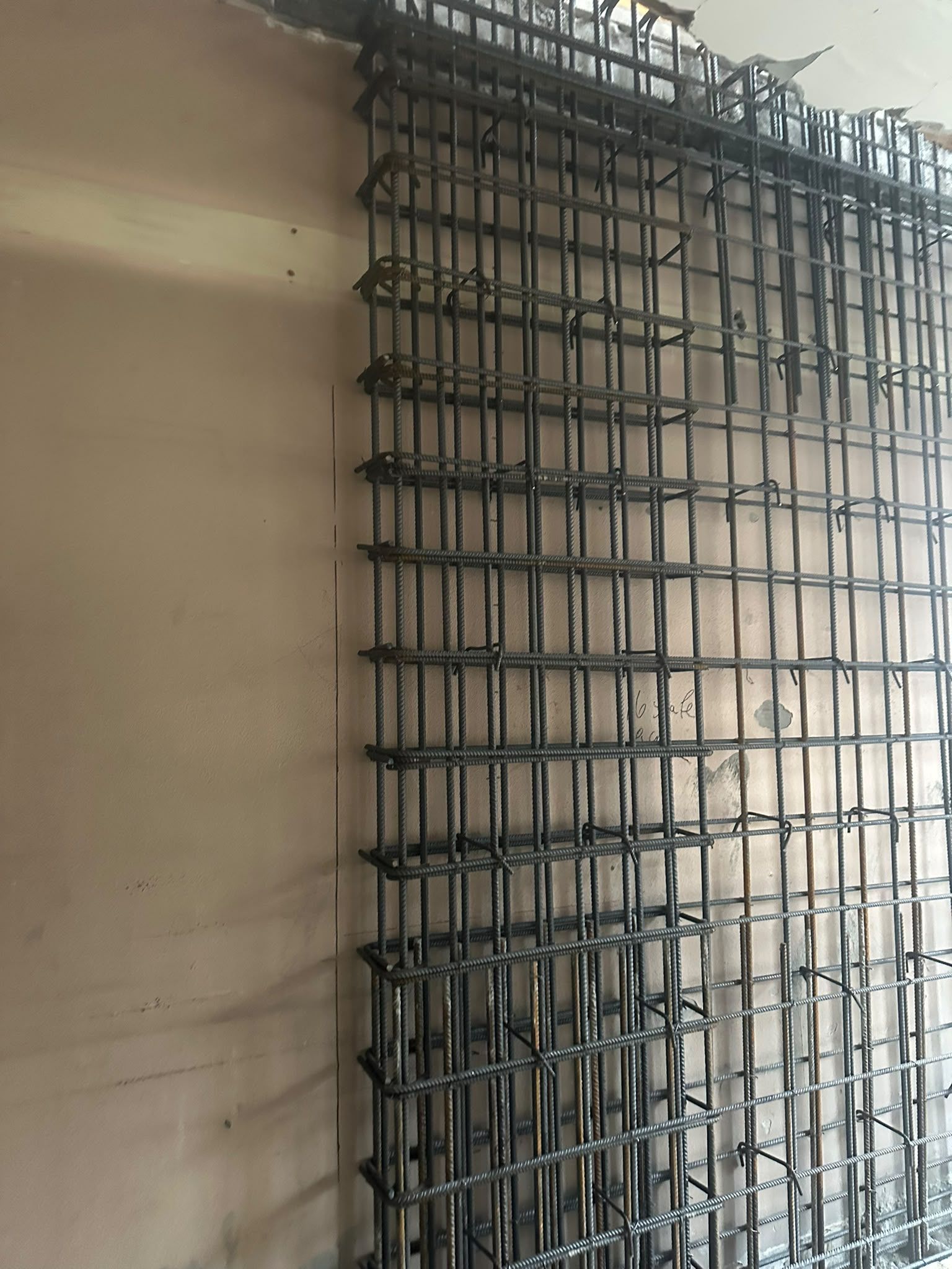 Rete di tondini d’acciaio contro una parete di cemento, a mostrare l’armatura di un edificio in costruzione.
