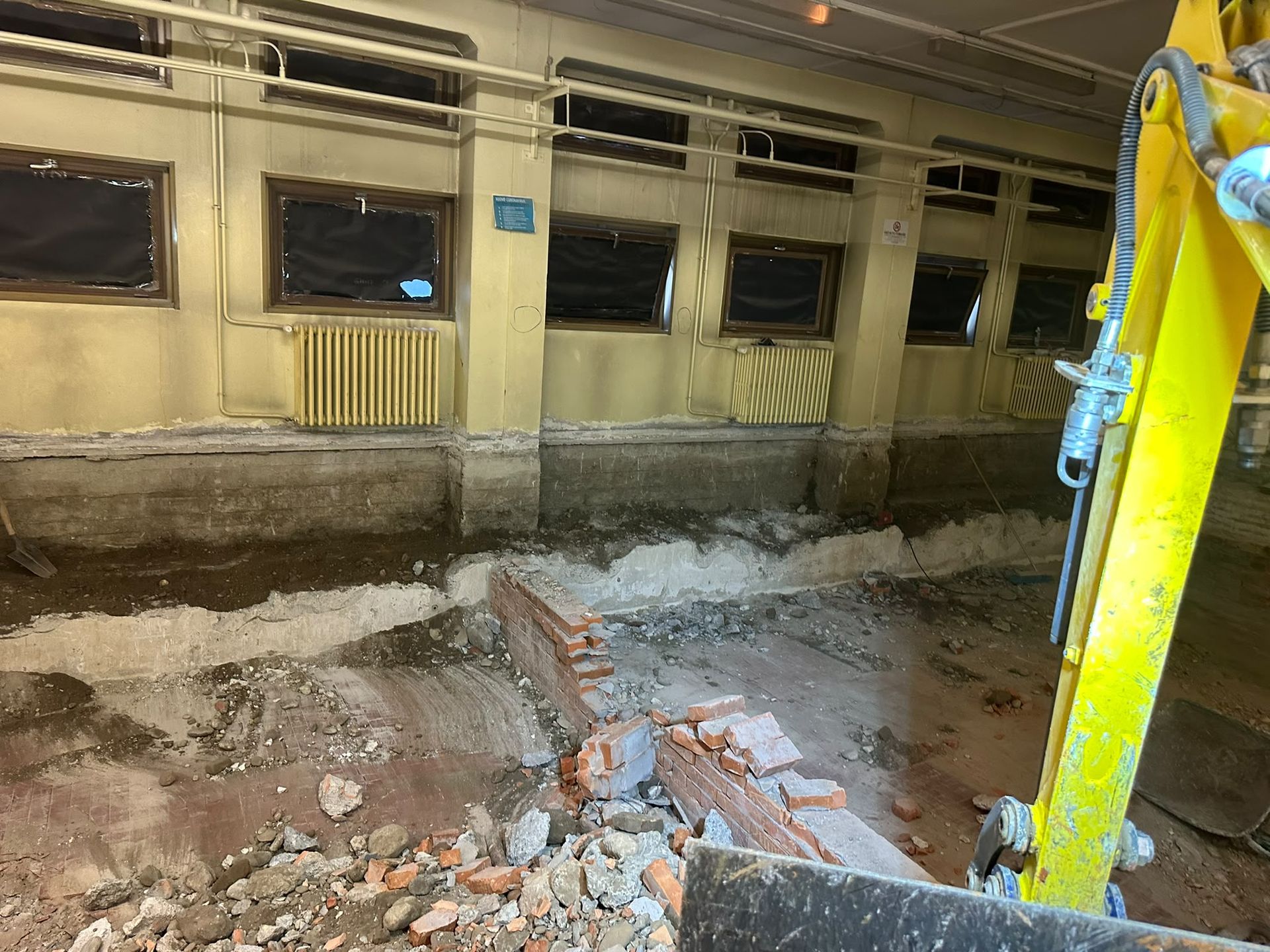 Macerie da demolizione all’interno di un edificio danneggiato, con pareti crollate, detriti e il braccio di un escavatore
