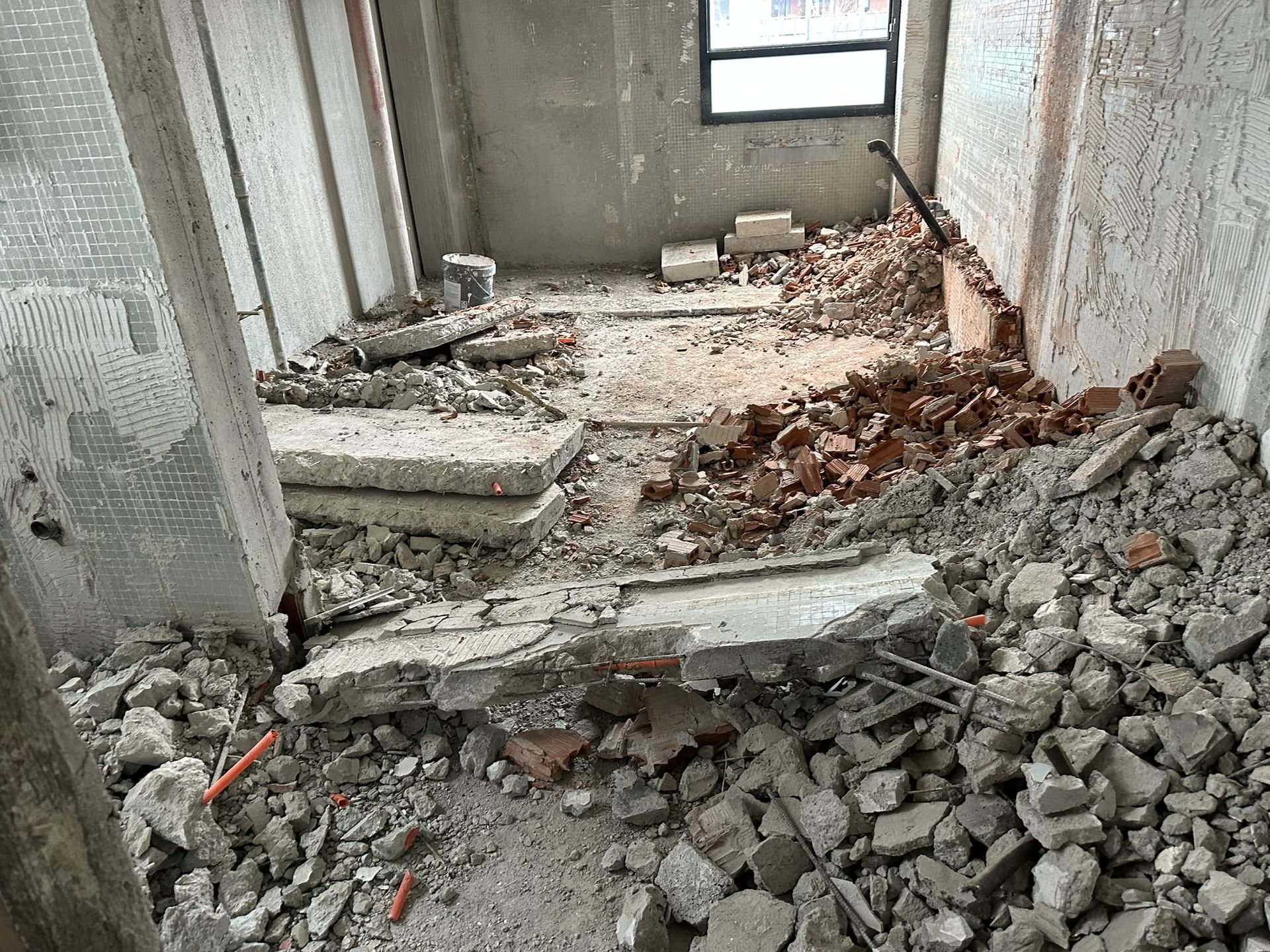 Corridoio danneggiato con scale di cemento rotte e cumuli di macerie in uno stretto passaggio interno