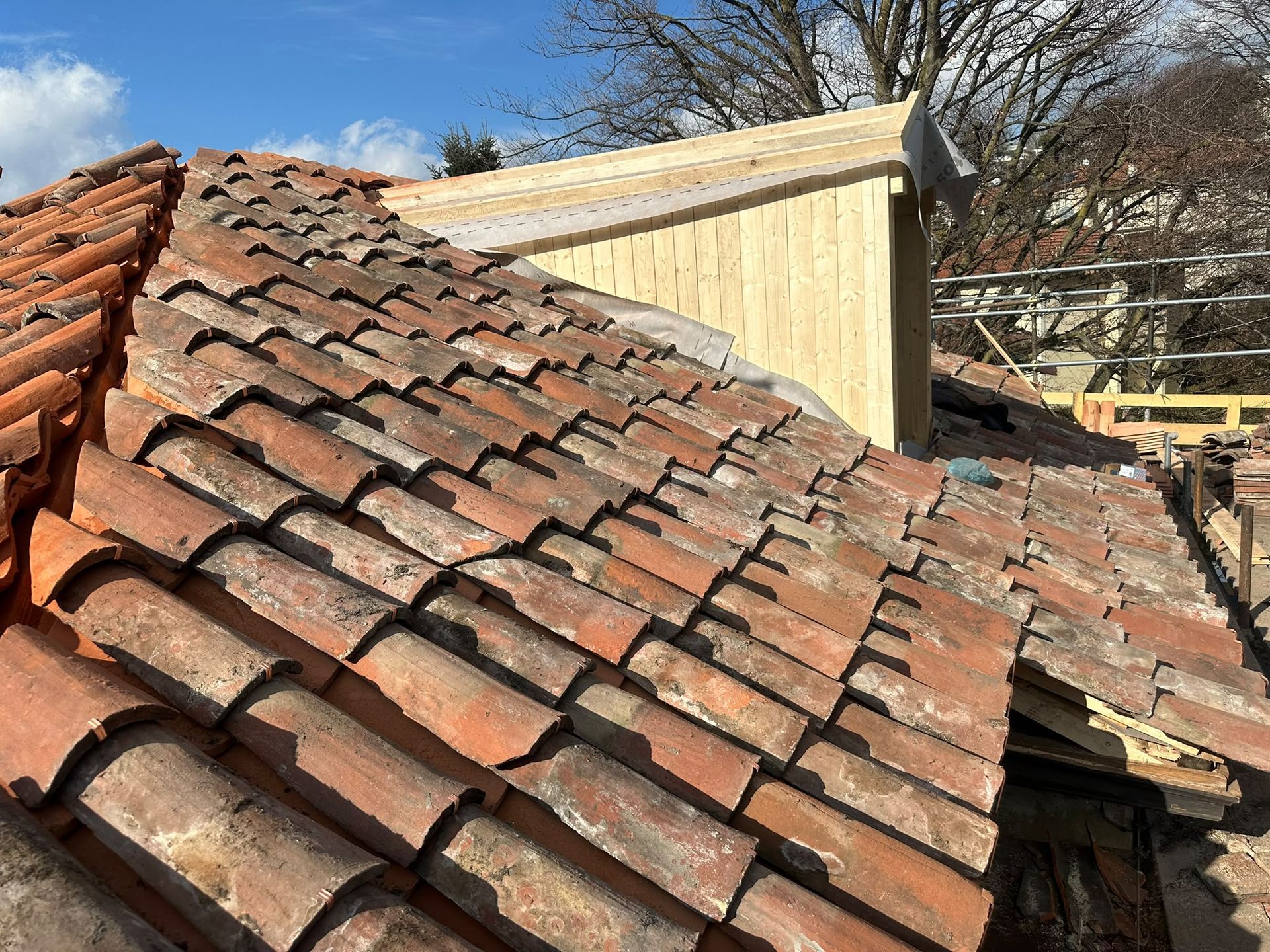Tetto in tegole di terracotta rosse crollato, con una struttura in legno danneggiata sullo sfondo