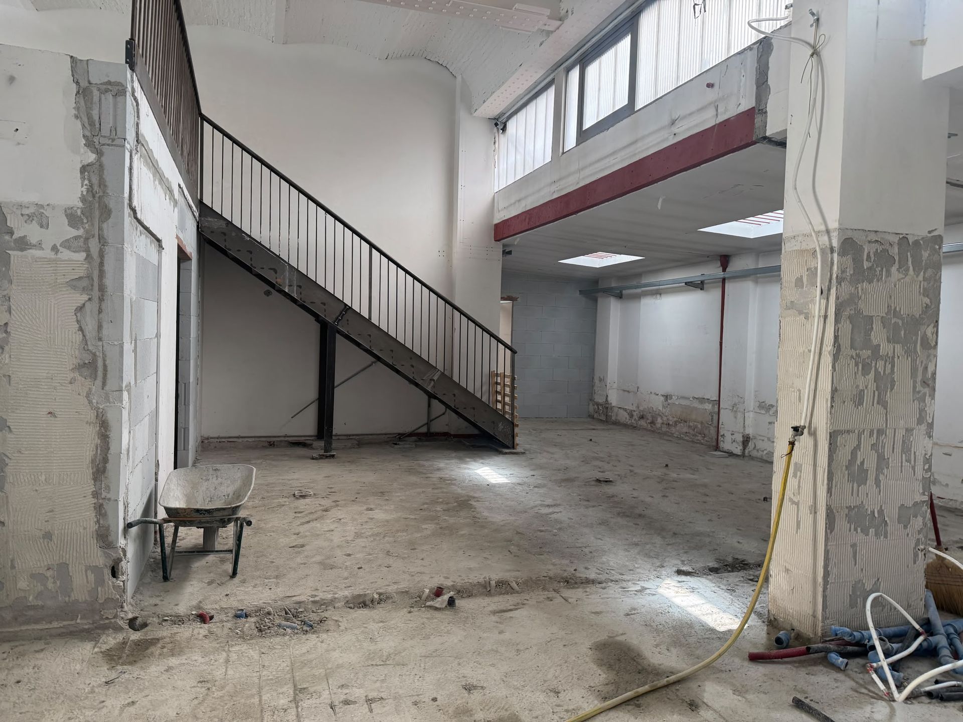Interno industriale vuoto con una scala metallica, pareti in cemento a vista e detriti sparsi sul pavimento