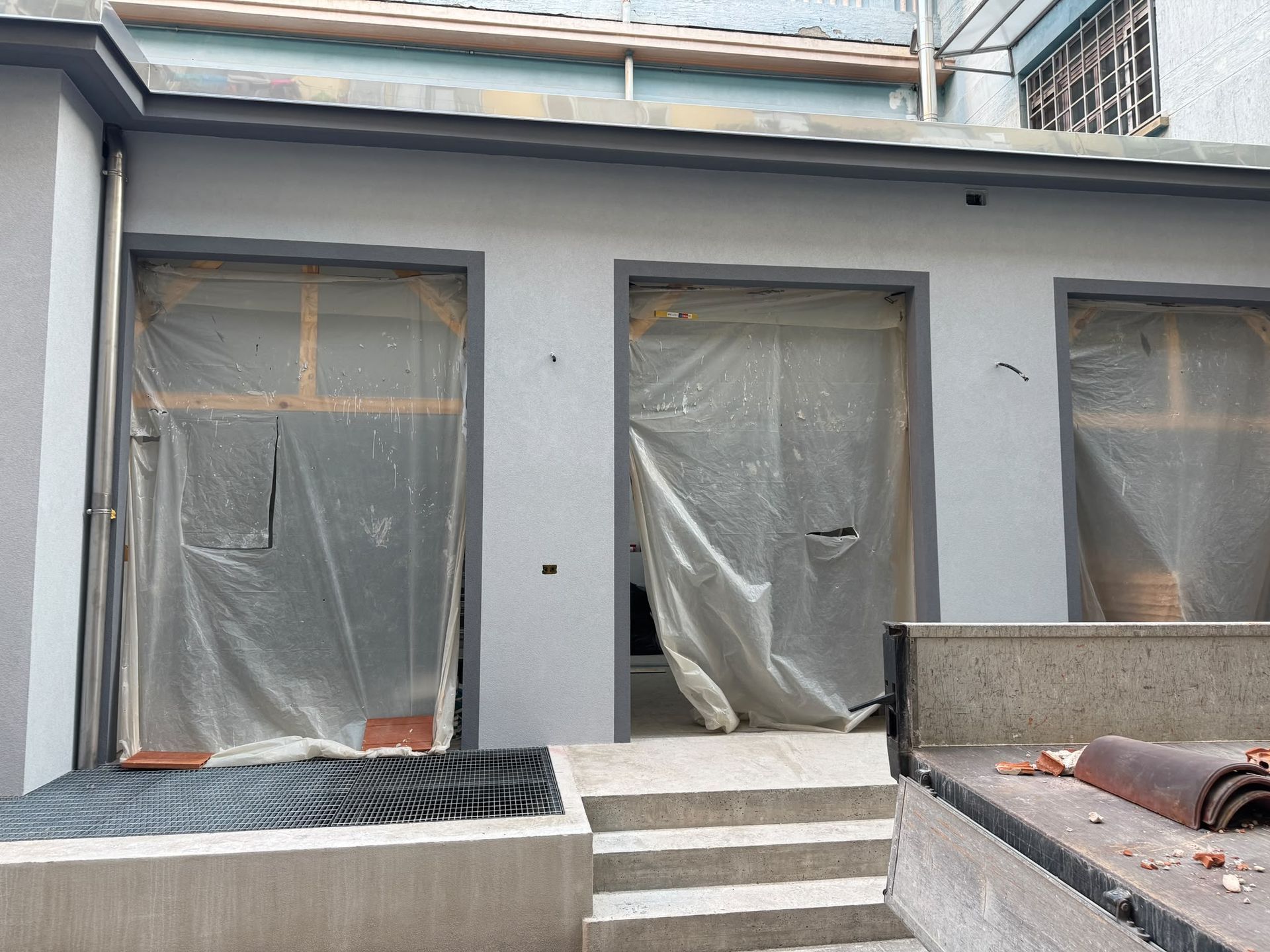 Facciata di una casa con tre finestre coperte con nastro adesivo e una piccola scalinata, in fase di ristrutturazione