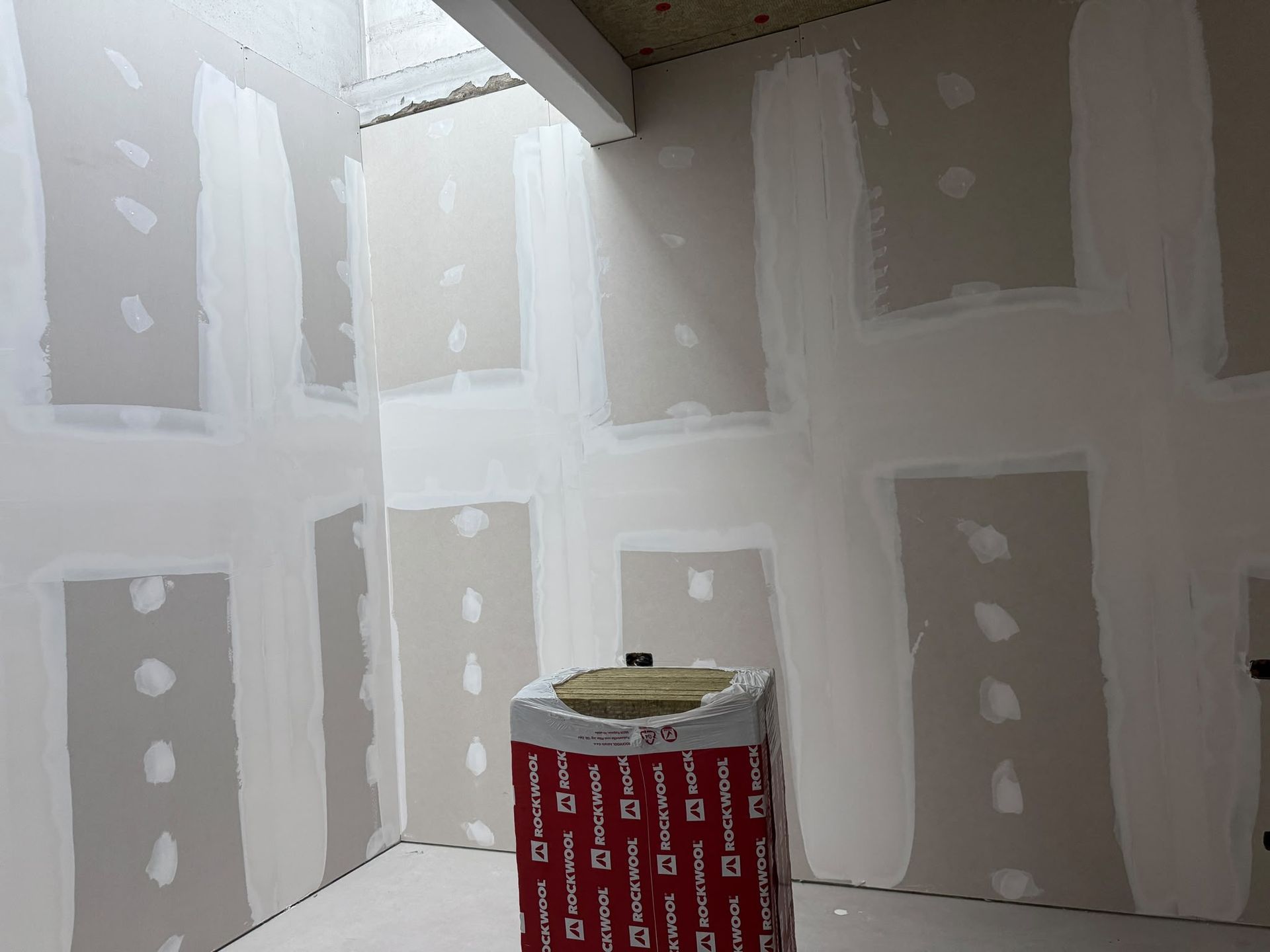 Stanza non finita con rattoppi in cartongesso e stucco per giunti, con un secchio di vernice in primo piano