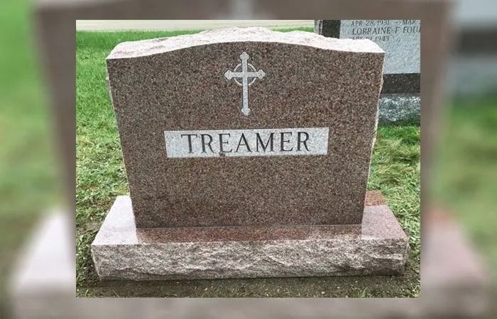 Brown granite gravestone with a cross and the name “TREAMER” in a grassy cemetery setting
