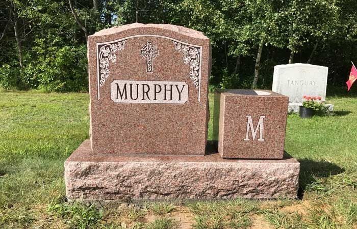 Pink granite memorial headstone engraved “MURPHY” with a smaller matching stone marked “M” in a grassy cemetery.