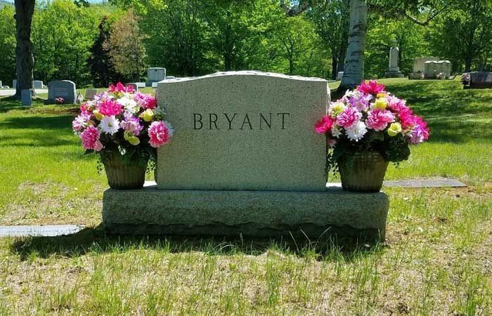 Bryant gravestone with pink flower arrangements in a sunny cemetery