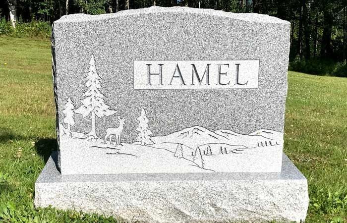 Gray granite memorial stone engraved “HAMEL” with a scenic etching, set on a grassy lawn.