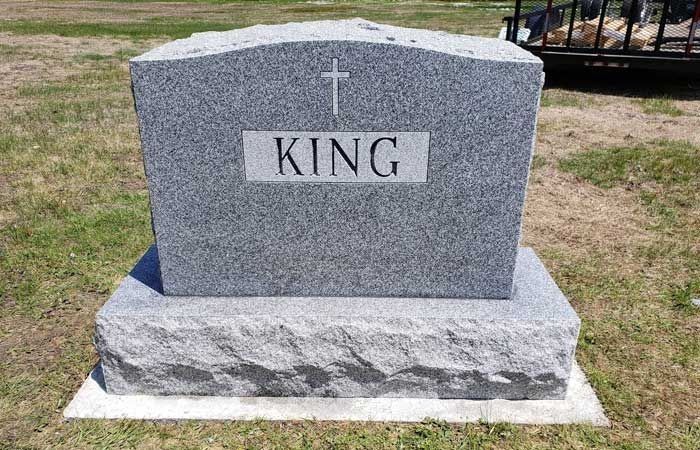 Gray granite gravestone with a cross and the name “KING” on a grassy plot.