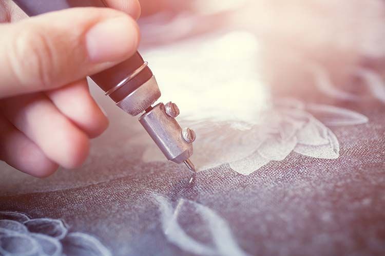 Hand using a wood-burning tool to engrave a floral design on a dark surface