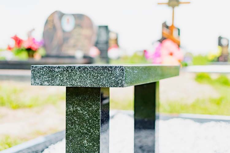 Stone bench in a sunlit park with blurred flowers and a fountain in the background