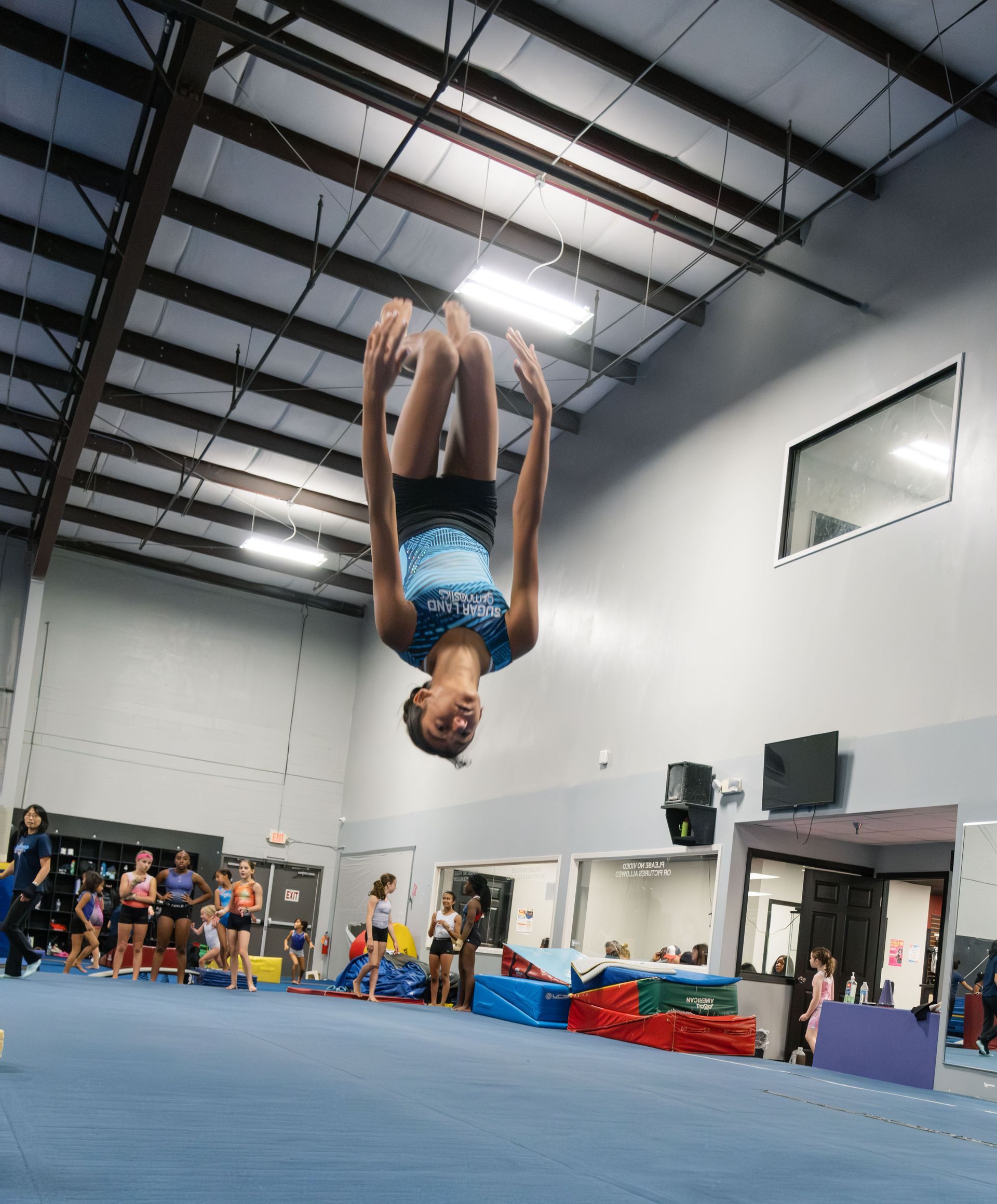 A girl is doing a handstand on a balance beam in a gym.
