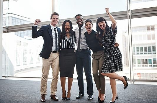 Five coworkers smiling and posing together in a bright office lobby