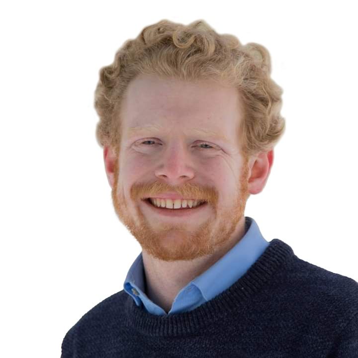 Smiling man with red hair and beard wearing a blue shirt and dark sweater on a white background