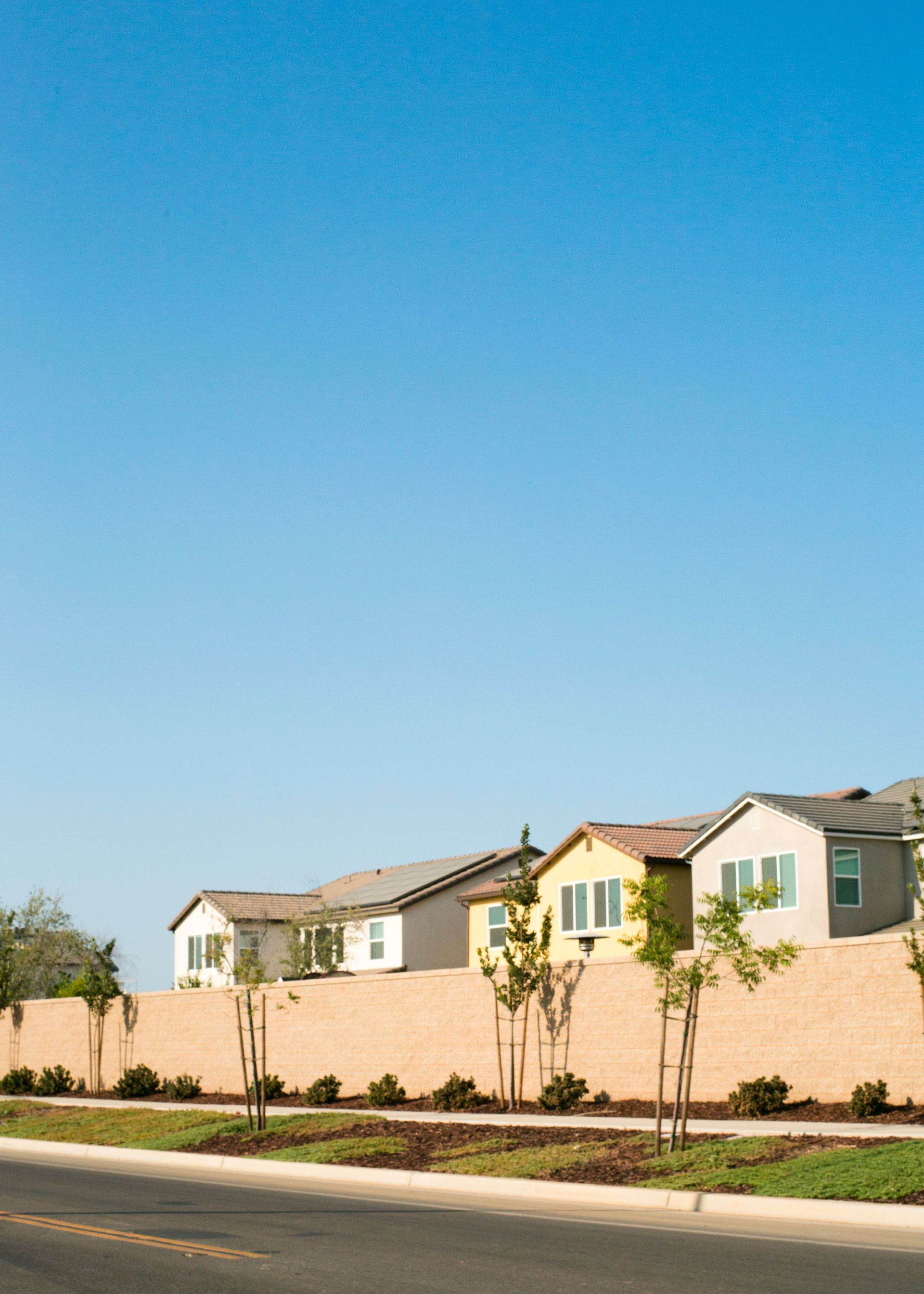 Row of suburban houses behind a tan wall under a clear blue sky