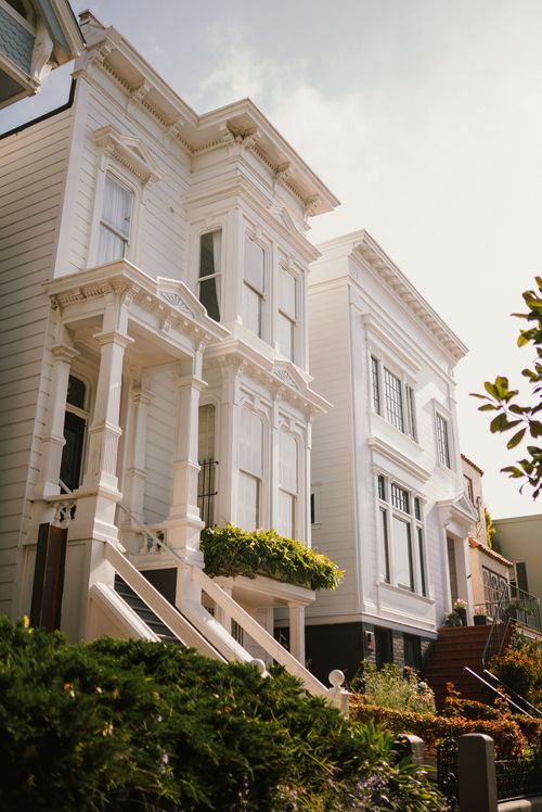 White row houses with ornate facades and front stairs on a sunny street.