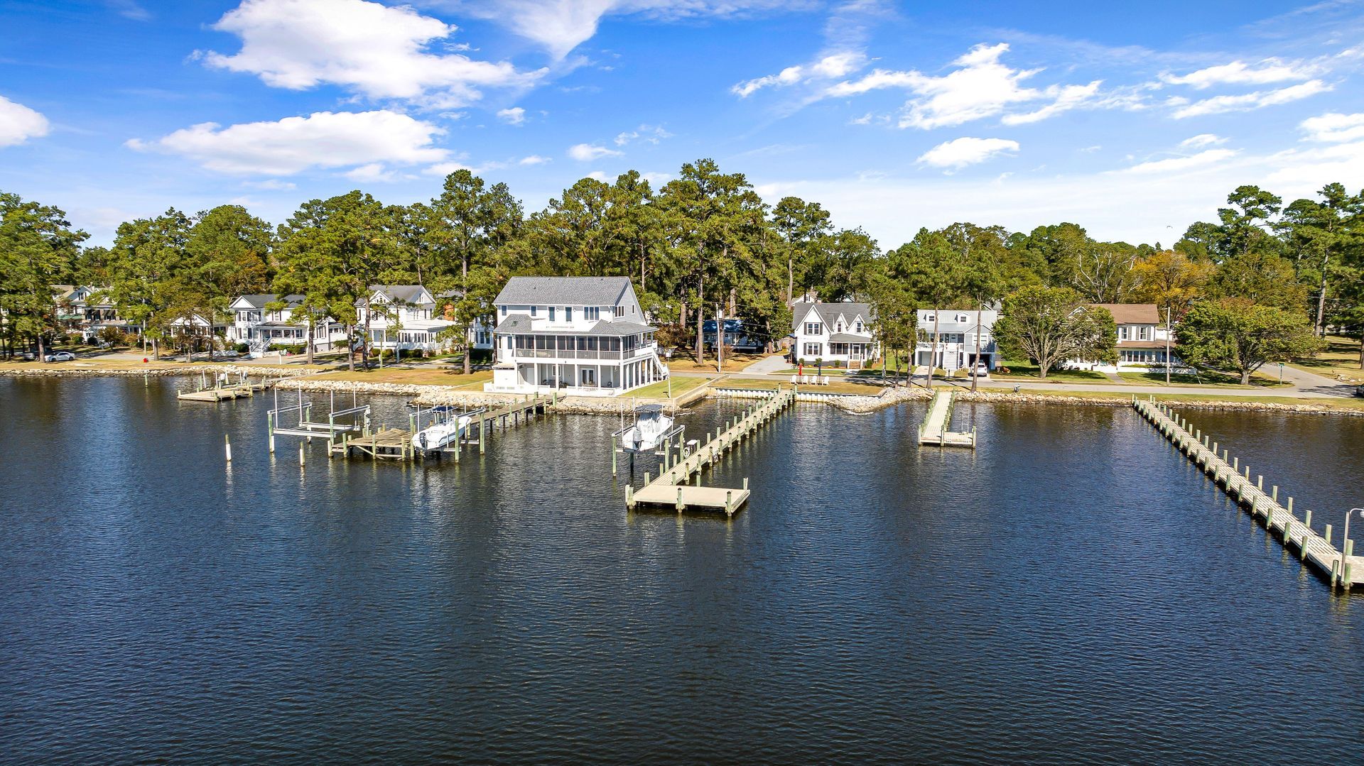 Coastal waterfront homes and docks along a calm bay with trees and blue sky