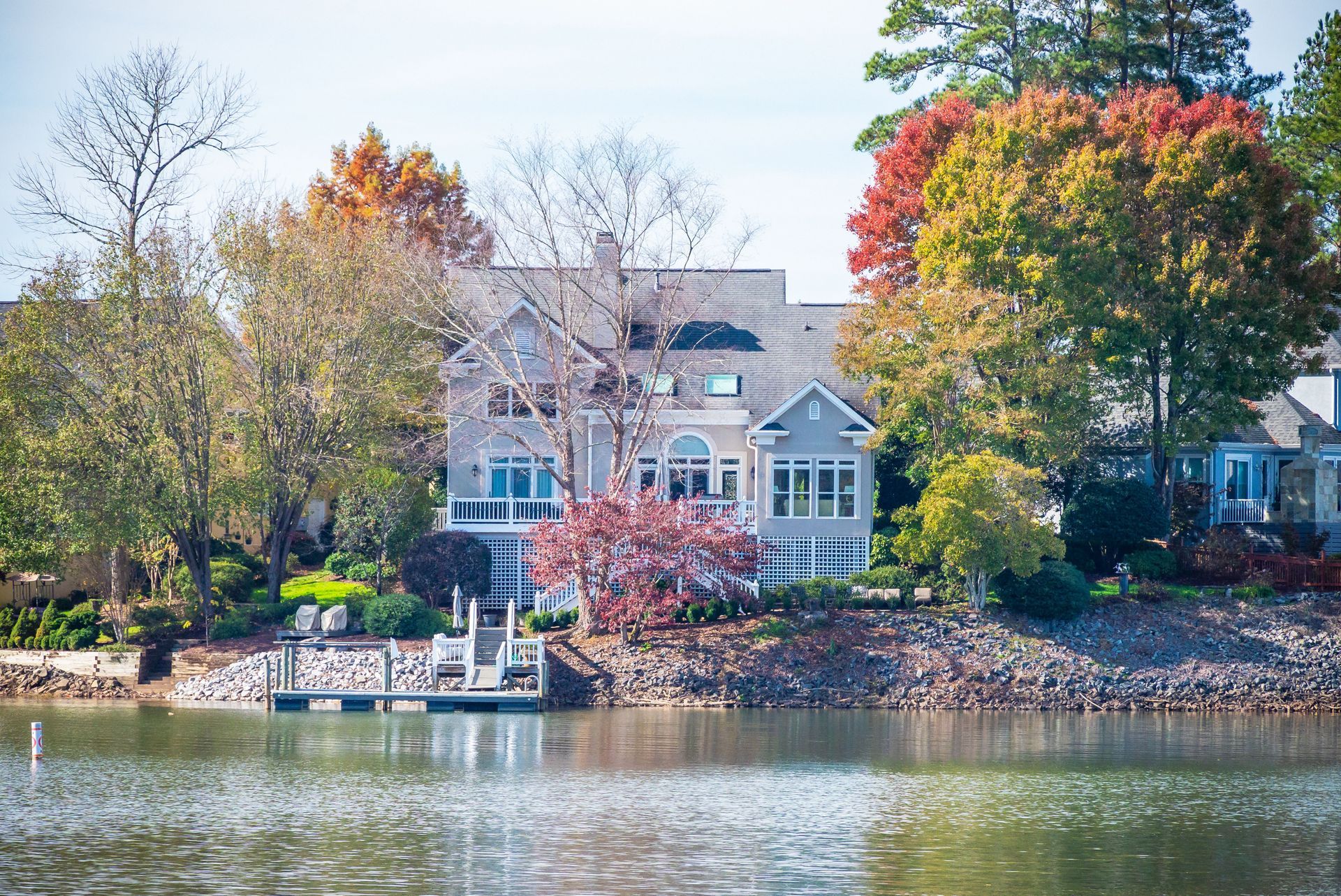 Lakeside house with a dock, framed by autumn trees and reflected in calm water.