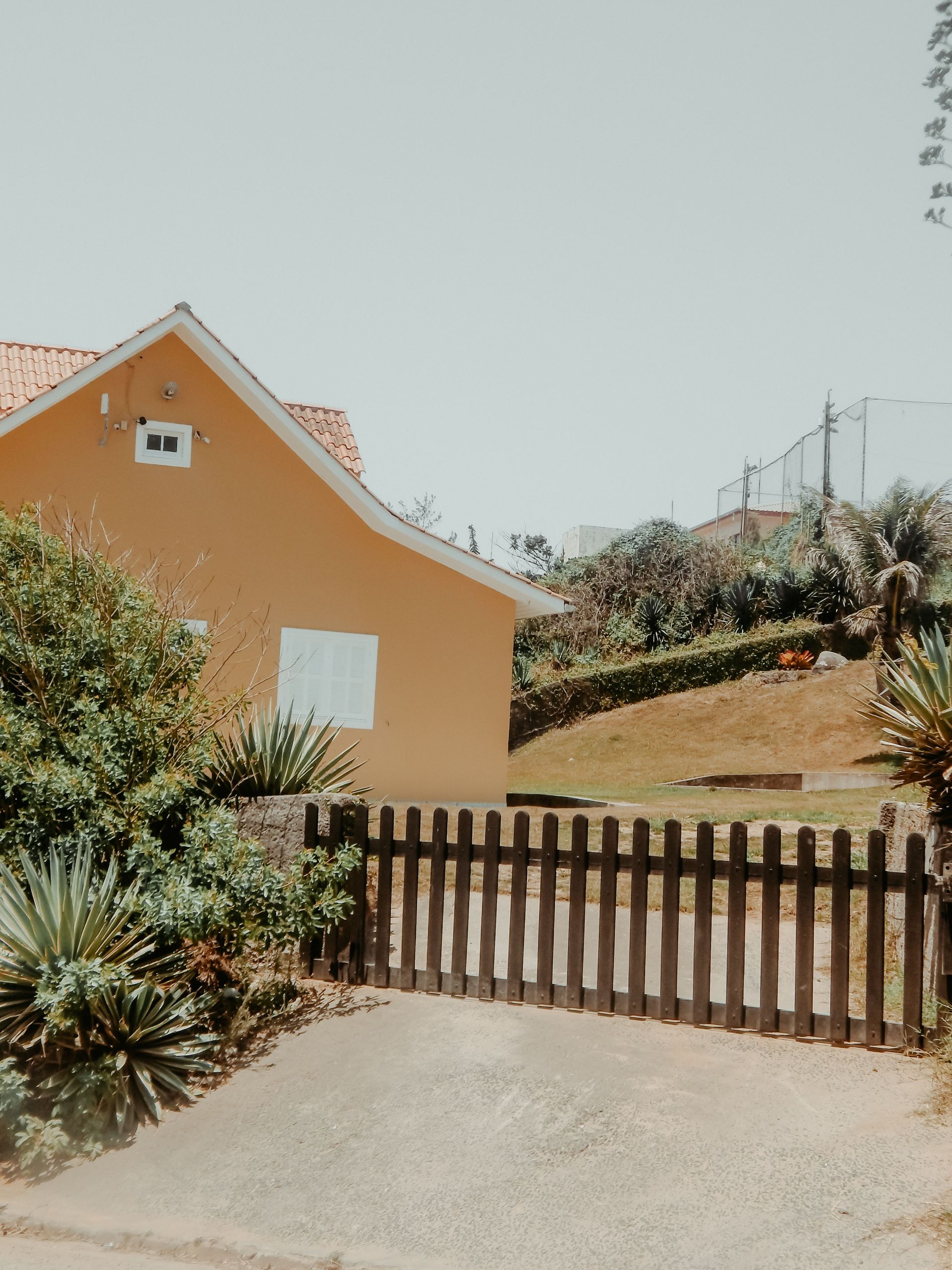 Orange house with tiled roof behind a wooden gate on a sunny hillside