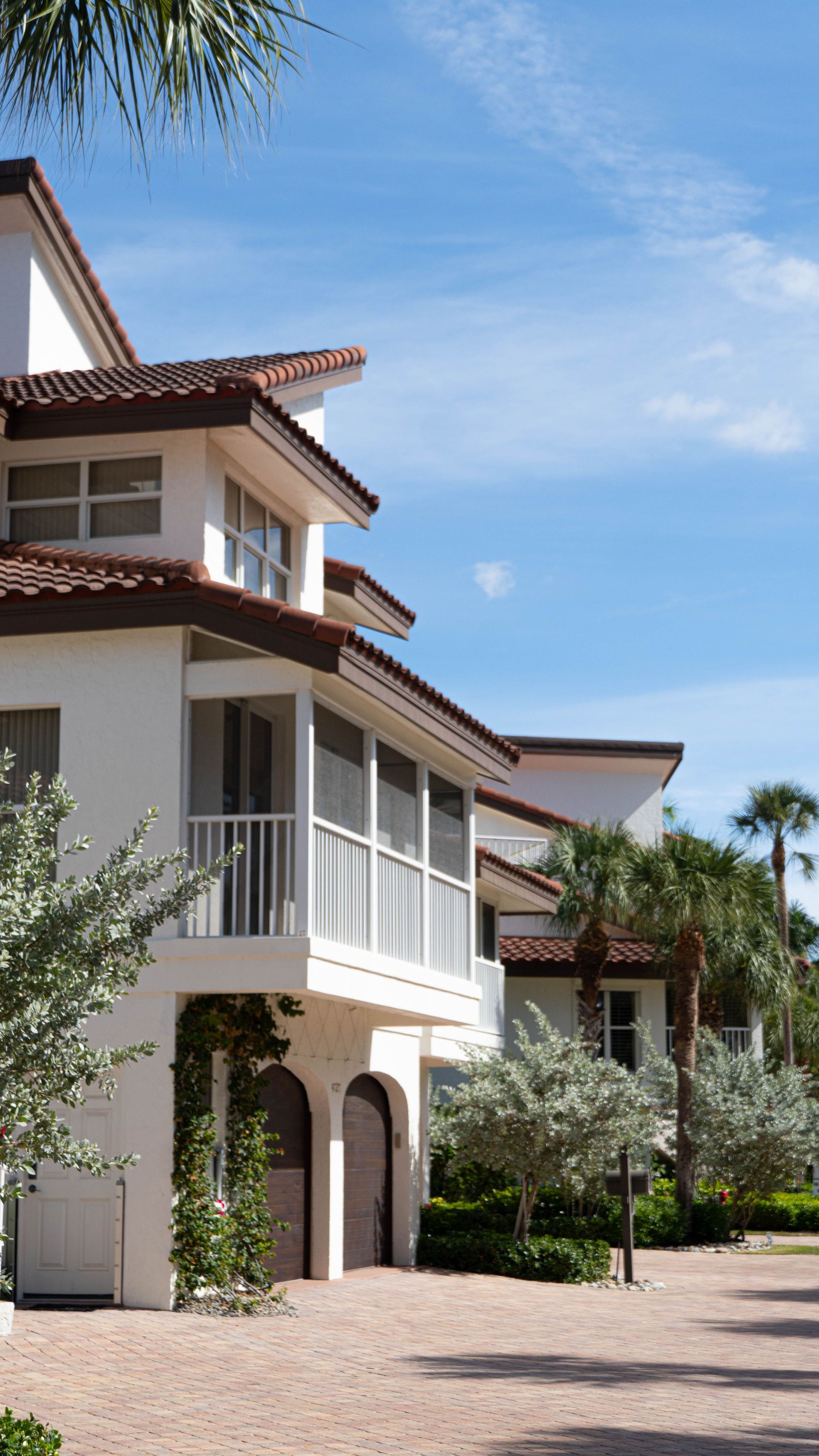 Sunlit Mediterranean-style apartment building with balconies and a courtyard walkway under a blue sky