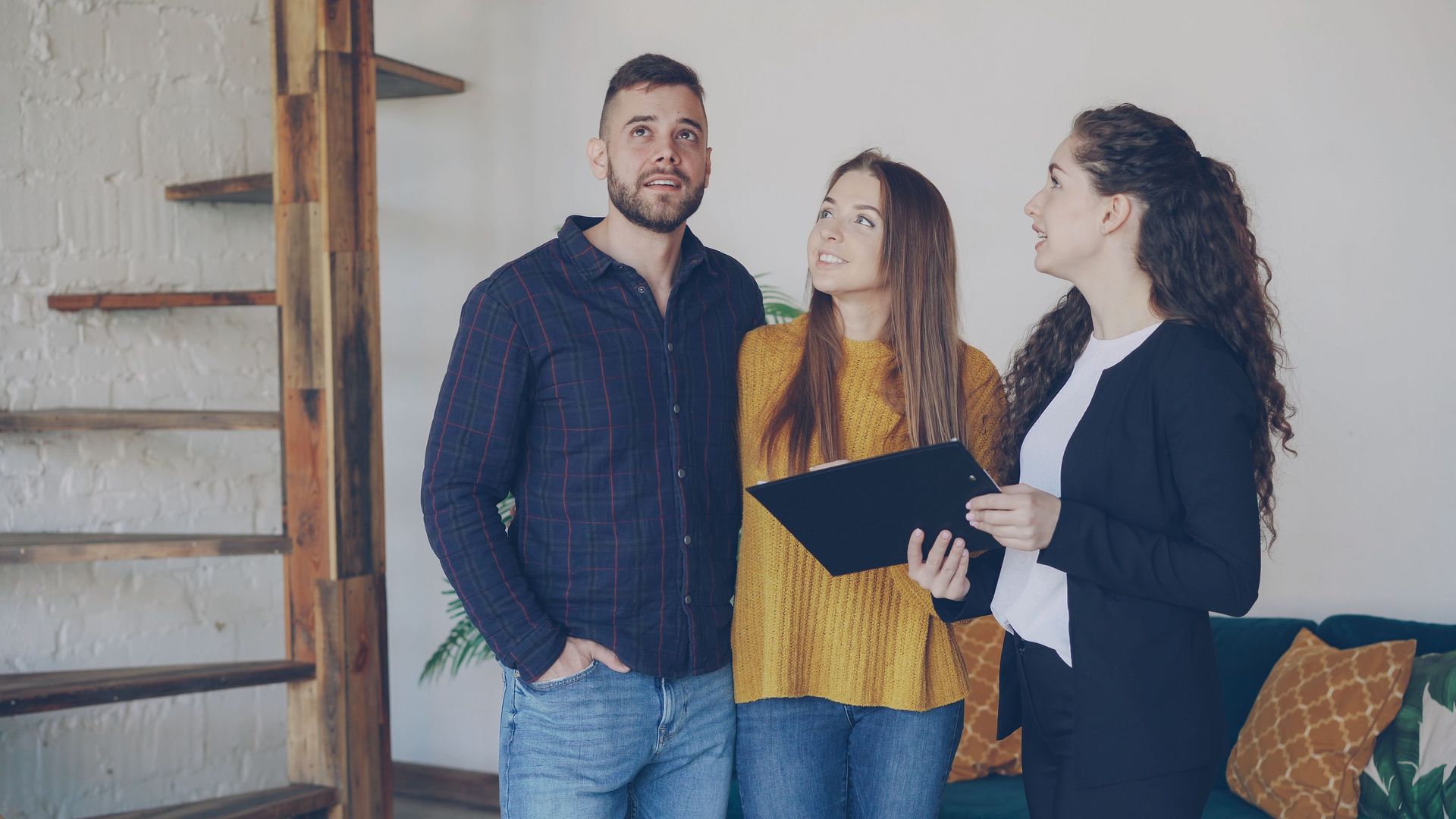 Three coworkers discussing a folder in a bright office near a staircase