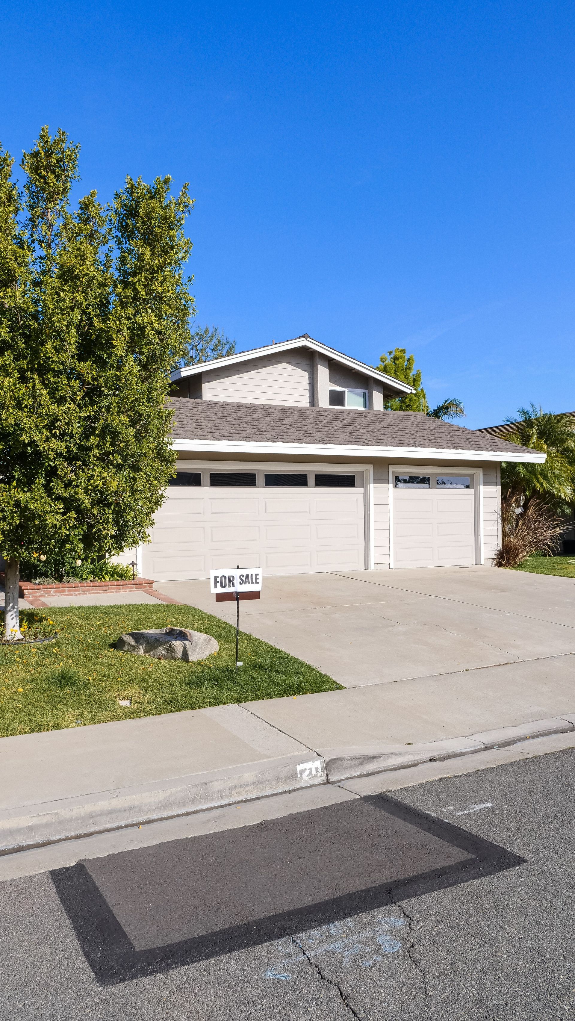 Suburban house with a two-car garage, front lawn, and tree under a clear blue sky