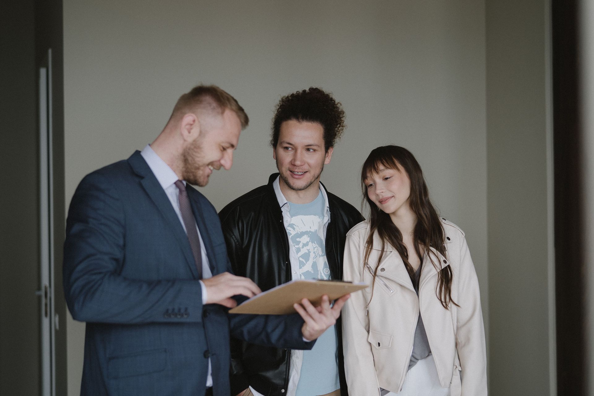 Three colleagues discussing a clipboard in a hallway, smiling and looking at documents.