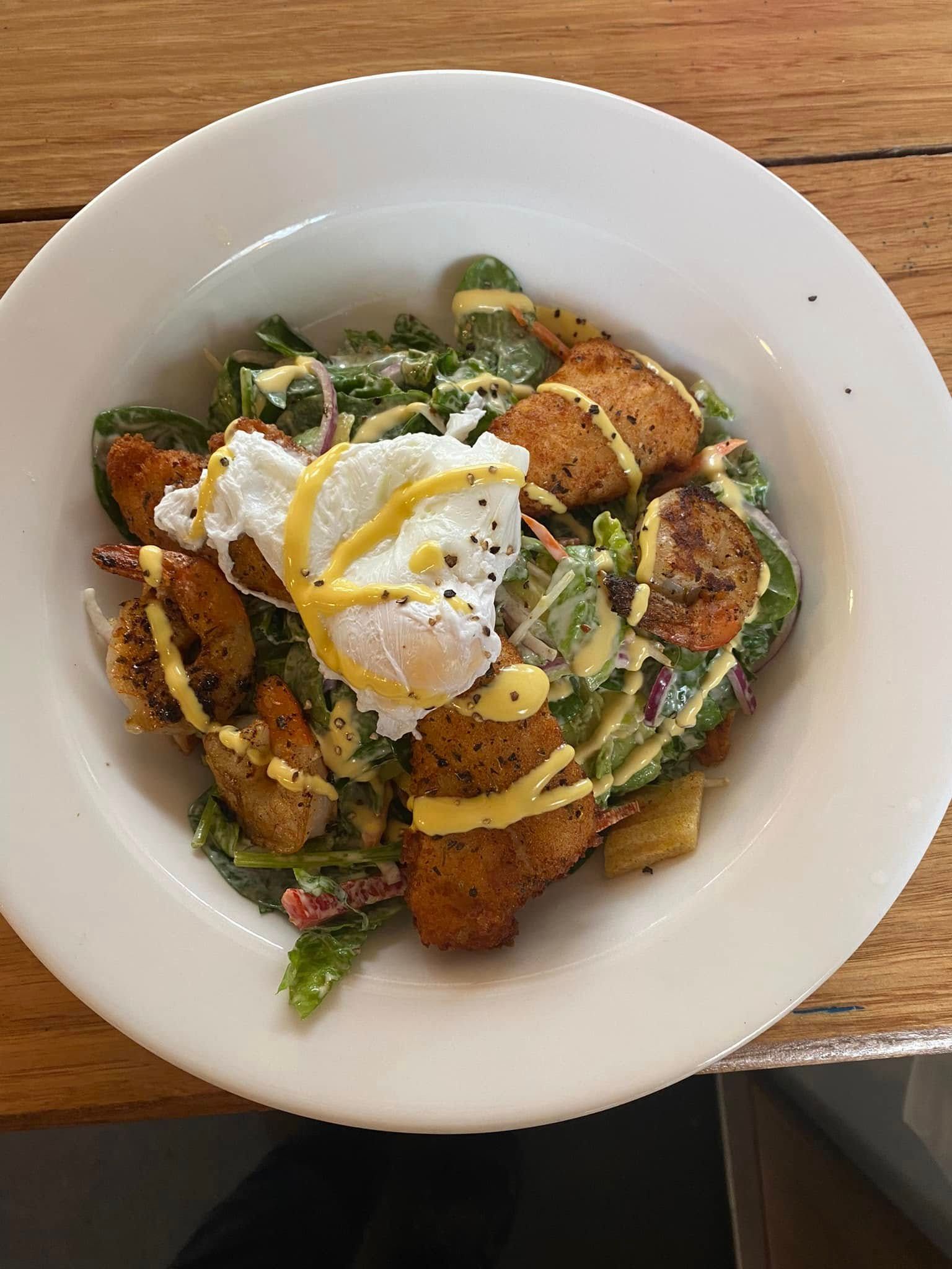 A salad in a white bowl topped with seasoned fried chicken, a poached egg, and a drizzle of yellow sauce. — 321 Cafe Learmonth In Learmonth, VIC