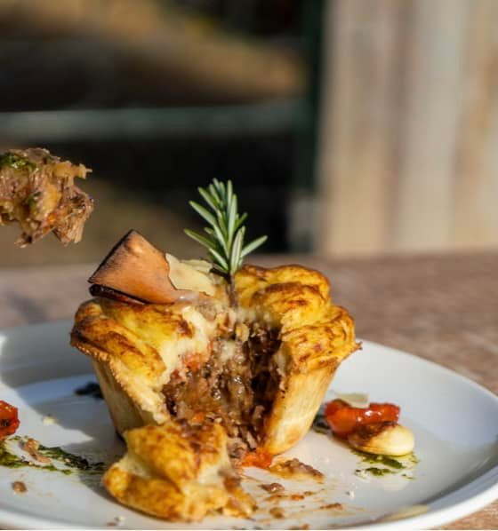A savory meat pie topped with a rosemary sprig, served on a white plate with small roasted tomatoes and herbs. — 321 Cafe Learmonth In Learmonth, VIC