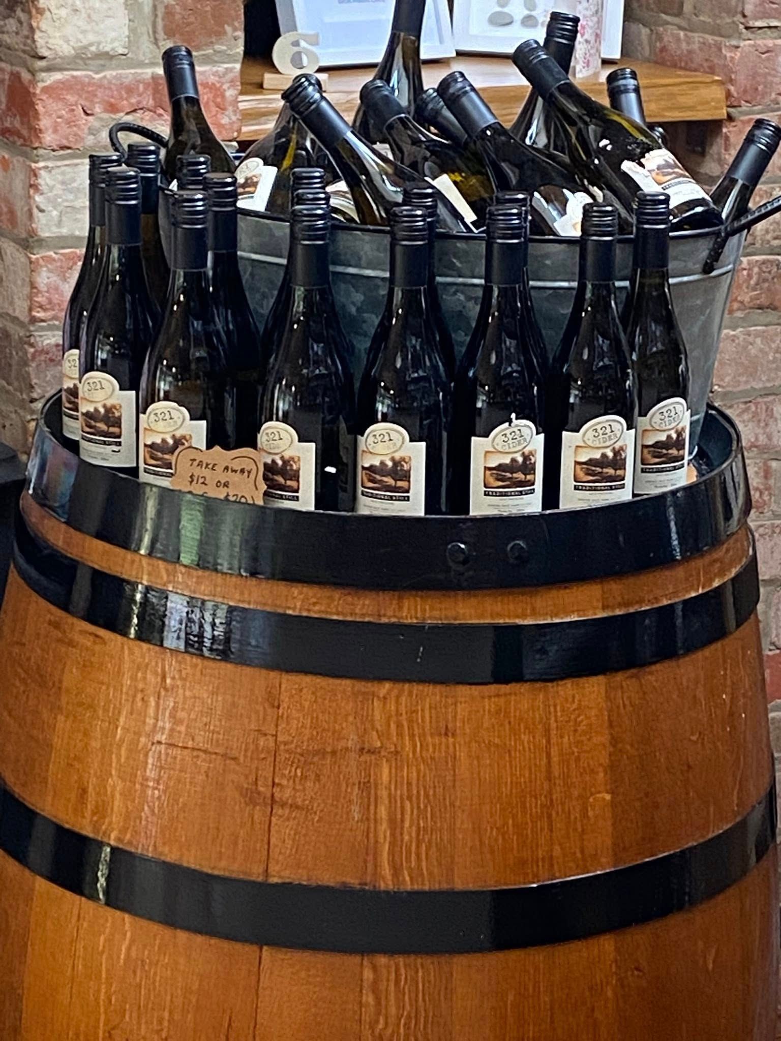 A metal bucket filled with wine bottles sits atop a wooden barrel against a brick wall. — 321 Cafe Learmonth In Learmonth, VIC