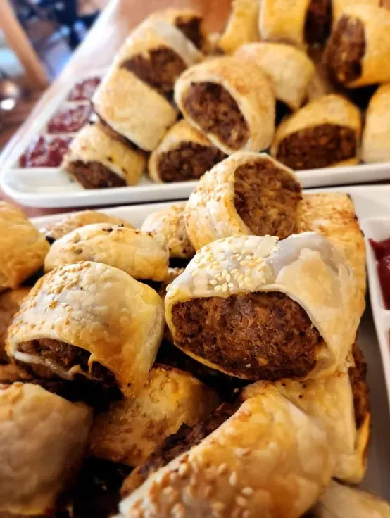 Two plates of golden-brown sausage rolls, some sprinkled with sesame seeds, with small portions of red dipping sauce. — 321 Cafe Learmonth In Learmonth, VIC