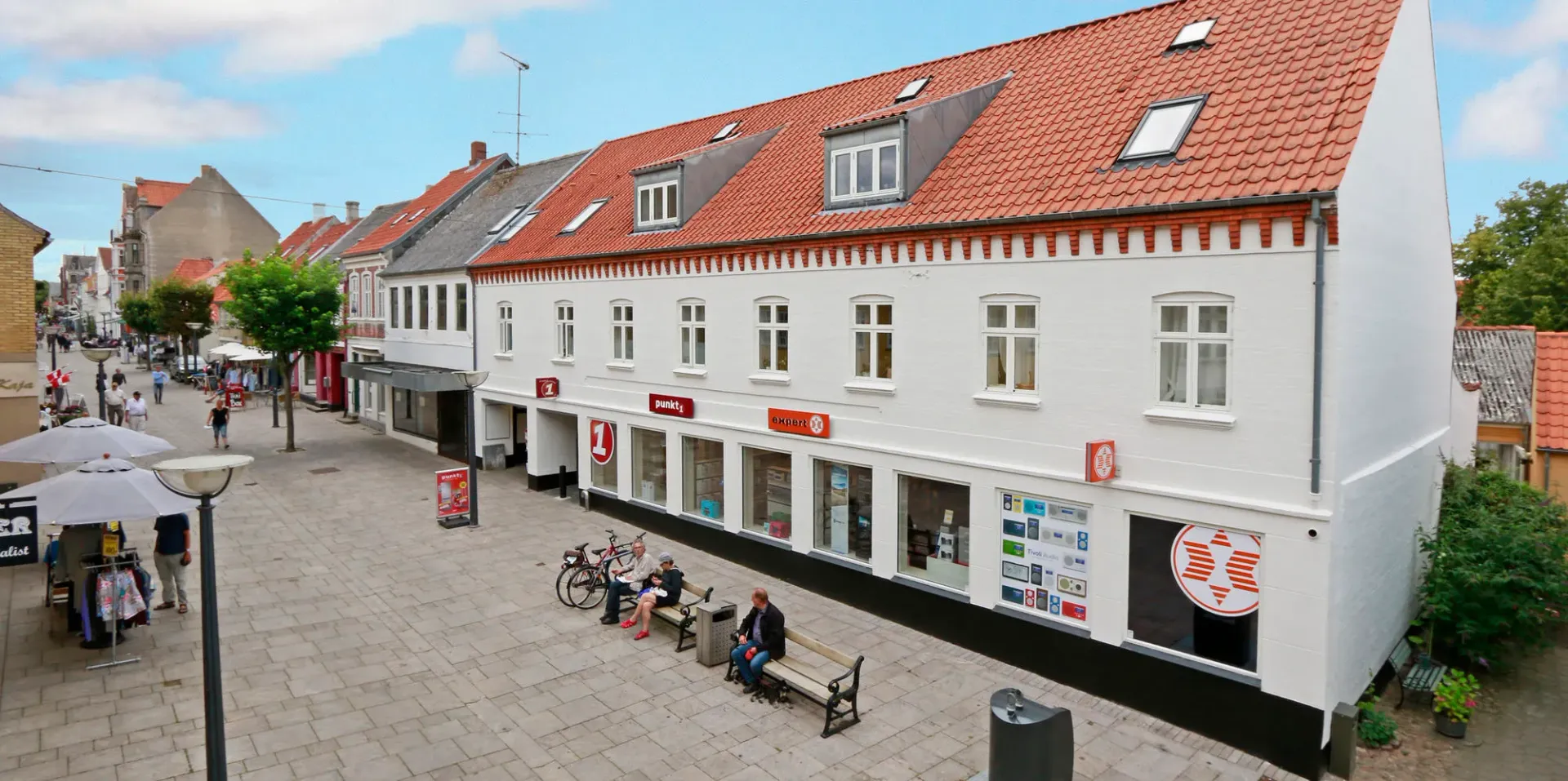 En gruppe mennesker sidder på en bænk foran en stor hvid bygning.