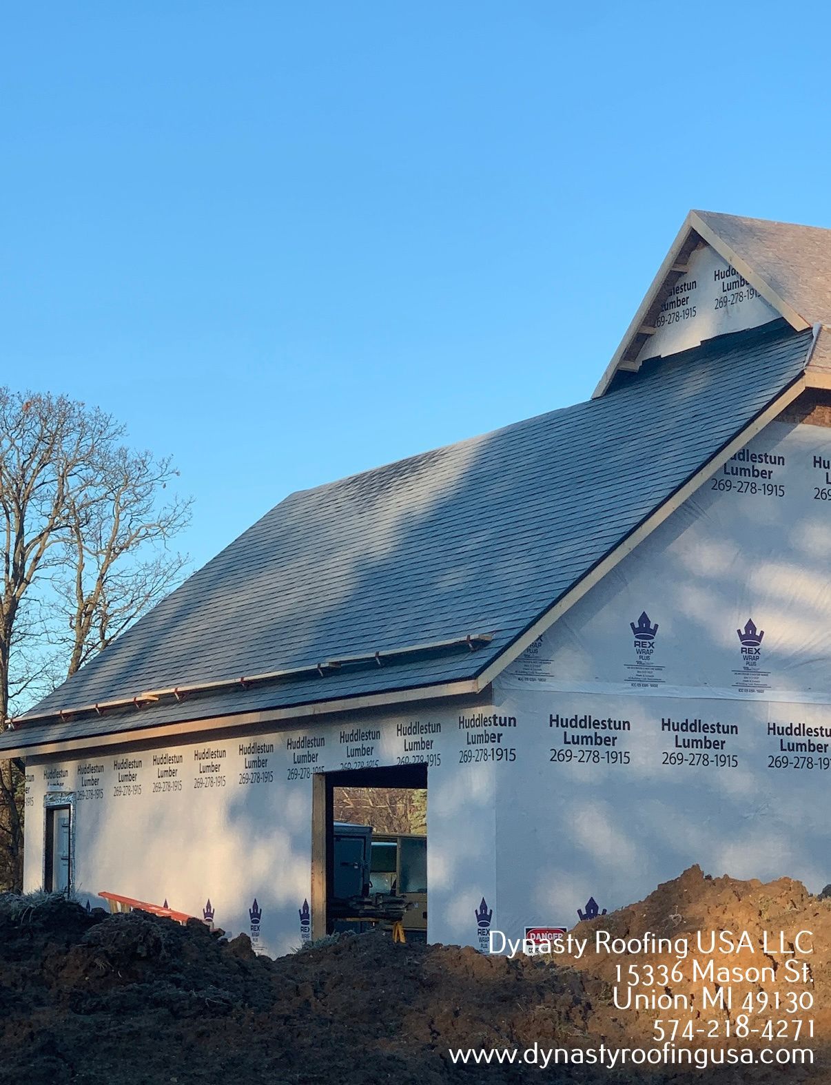 Building under construction, with a partially completed gray shingle roof and white protective wrap on the walls.