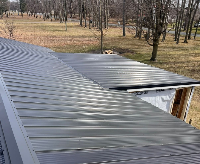 Metal roof installation on a building with a grassy landscape background.