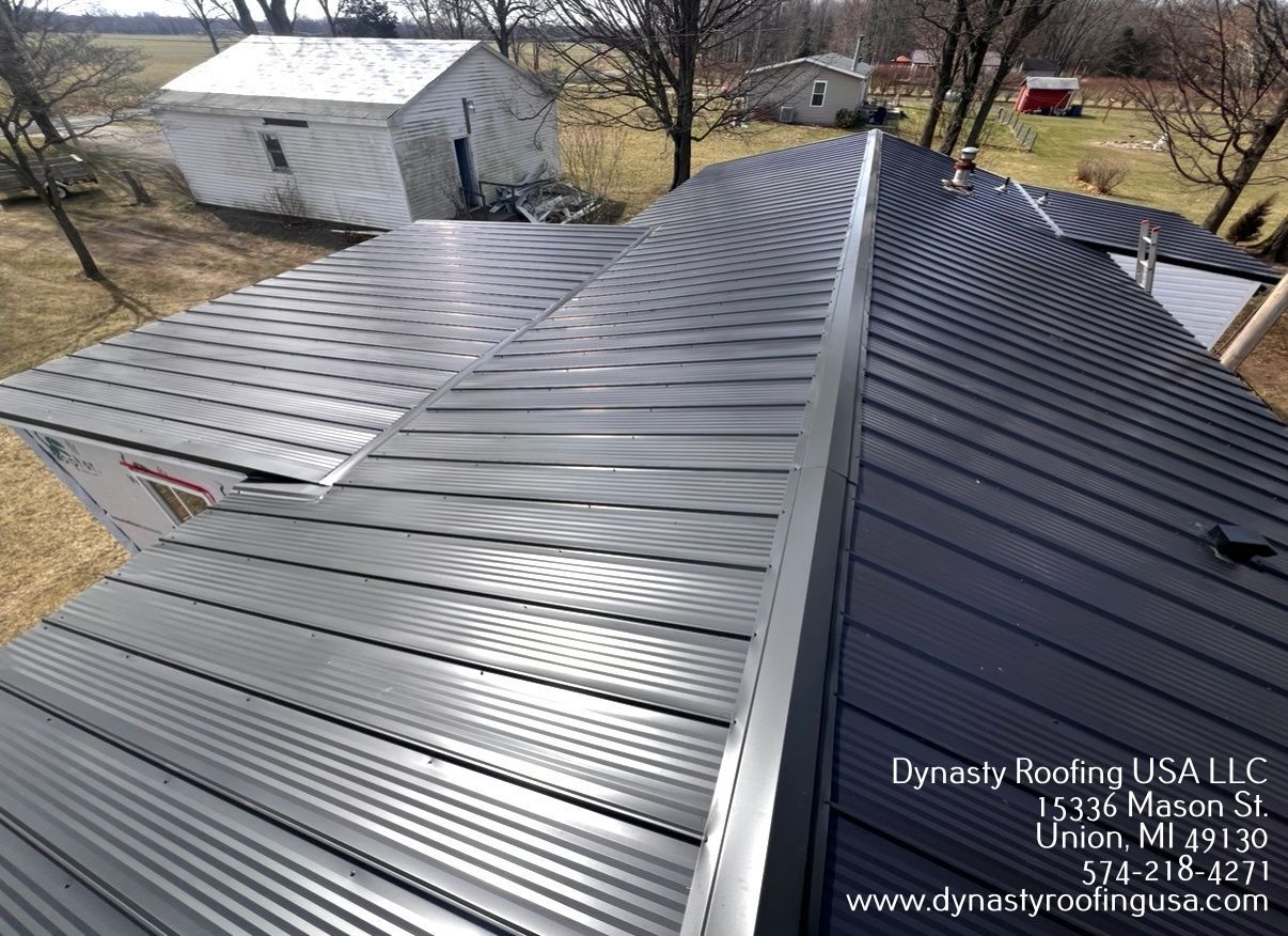 An elevated view of a newly installed dark metal roof on a house, with contact information for Dynasty Roofing in the corner.