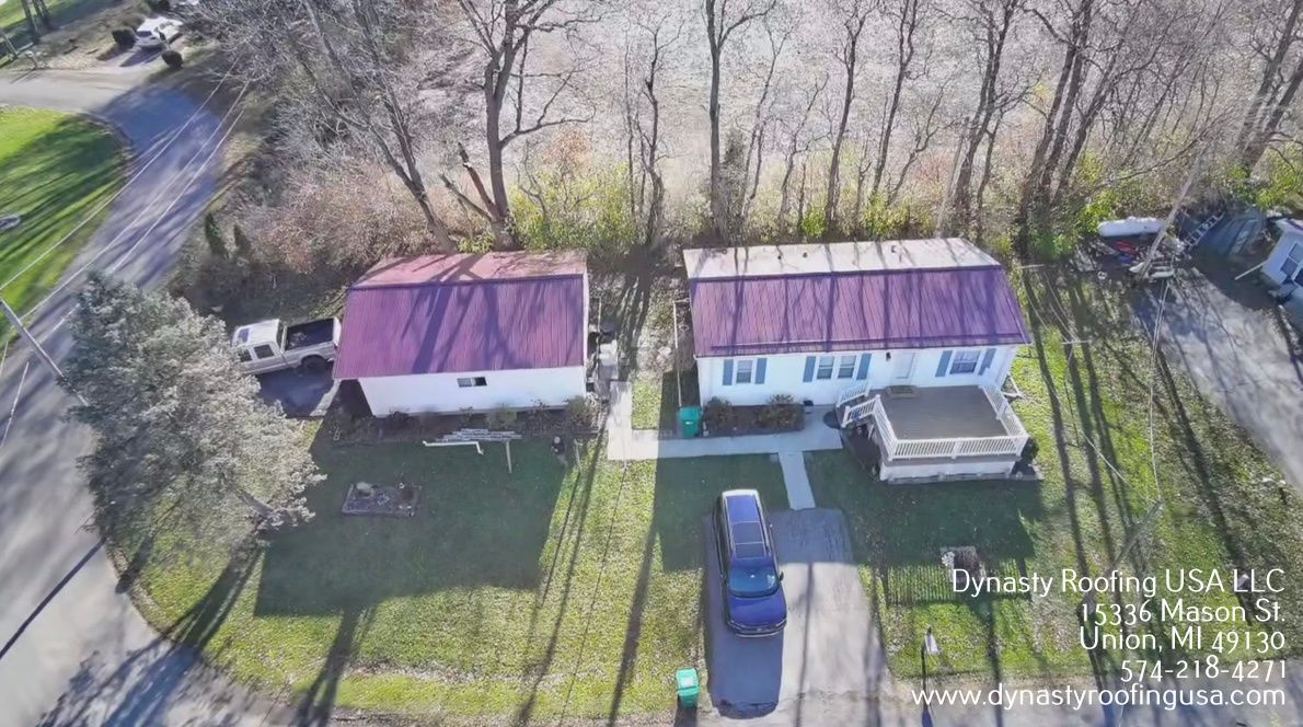Aerial view of two small houses with red roofs and a driveway lined by trees.