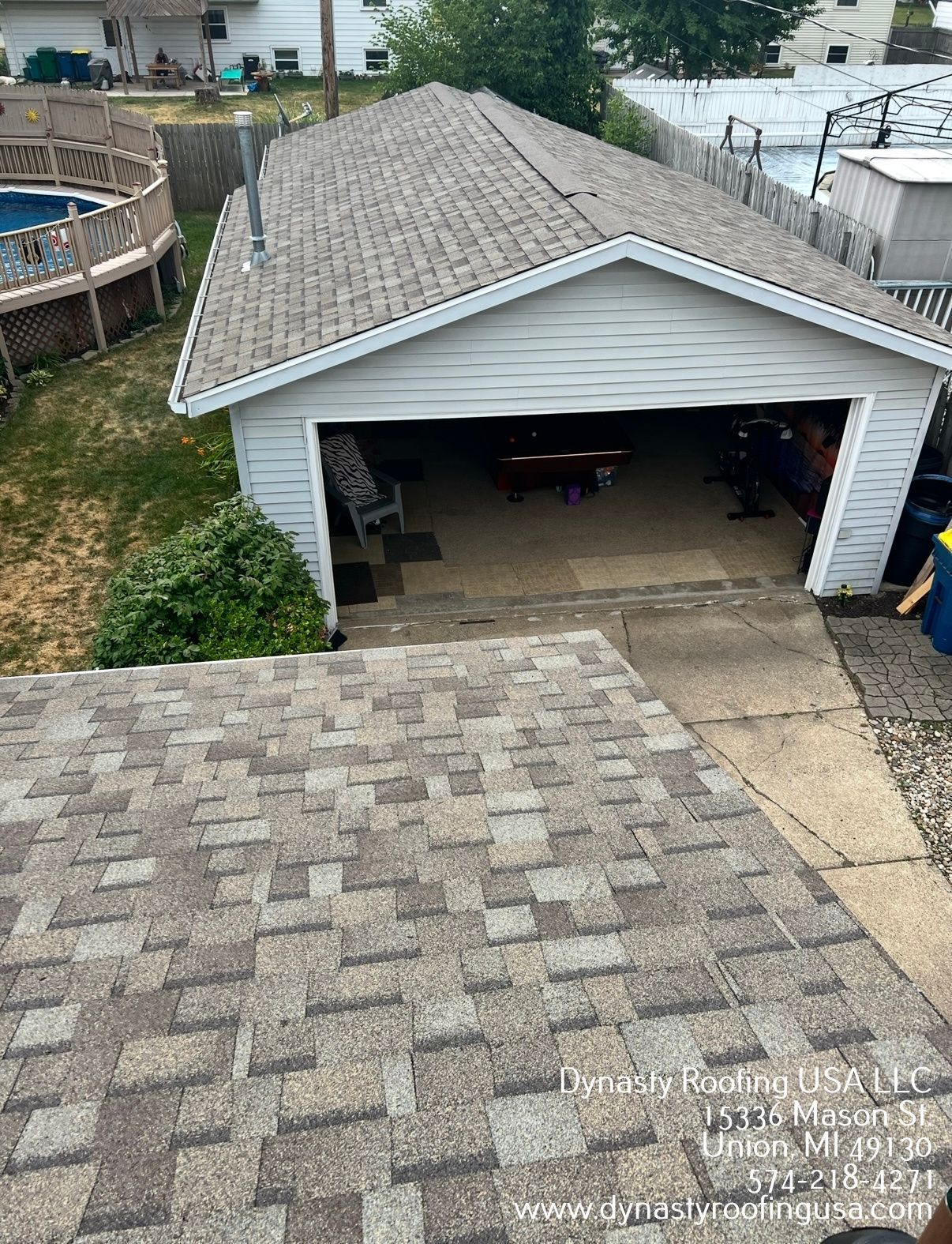 Overhead view of a garage with a new shingle roof. The garage door is open, and a swimming pool is visible.