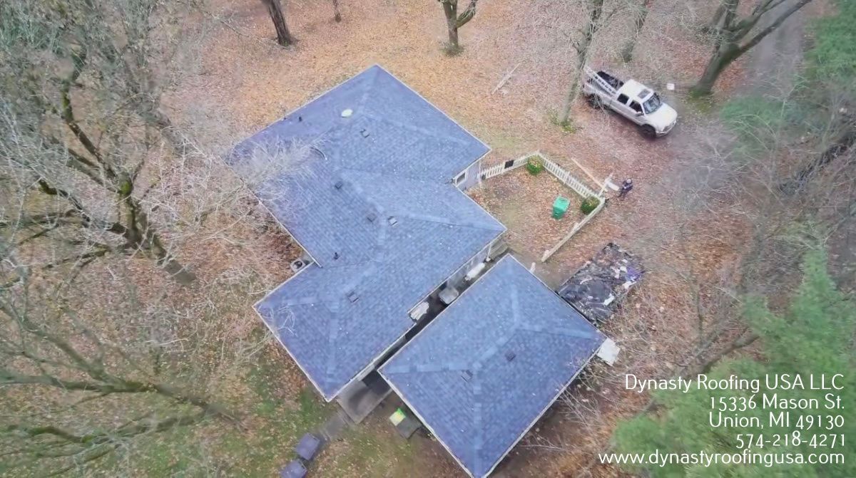 Overhead view of a house with a dark gray roof surrounded by trees and a white truck.