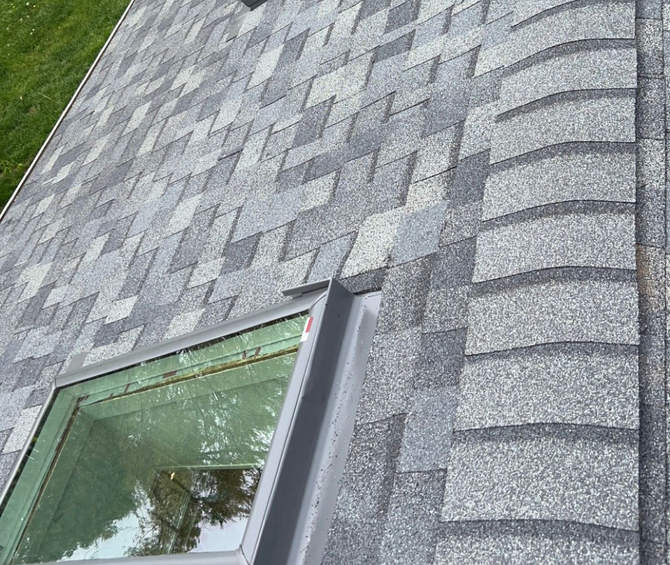 Gray asphalt shingle roof with skylight; close-up view outdoors.