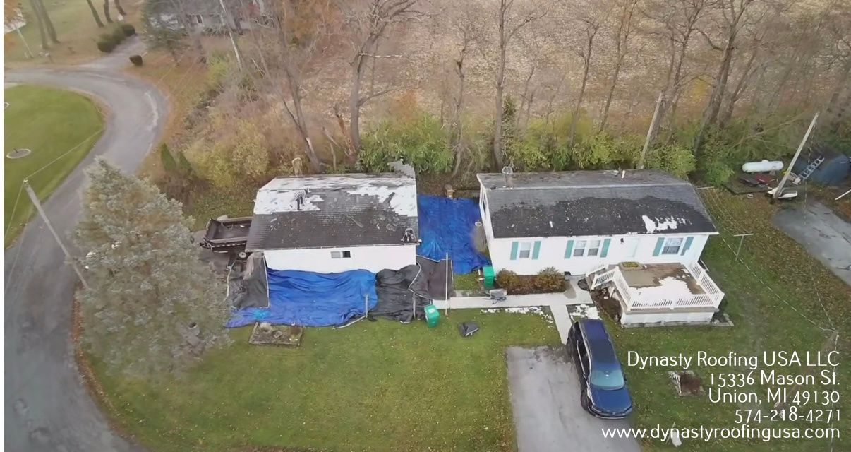 Aerial view of two homes, one with blue tarp covering damaged roof.
