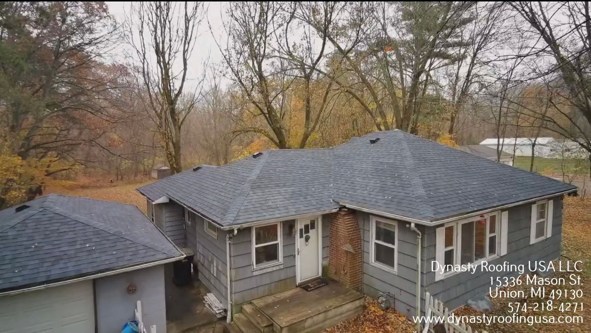 Gray house with dark roof, surrounded by trees in autumn.