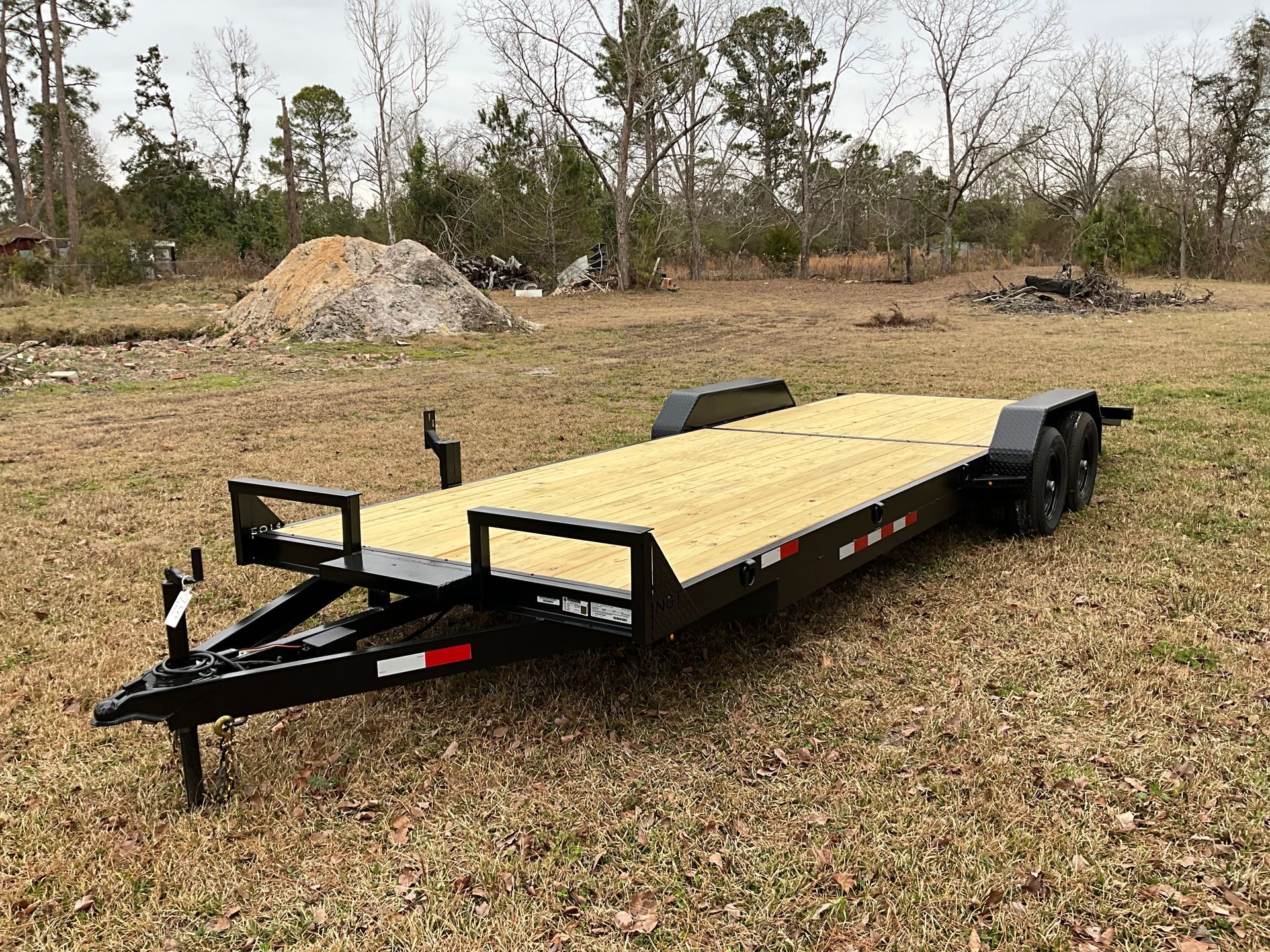 A new black tandem-axle car hauler trailer with a light-wood deck parked in an open field.